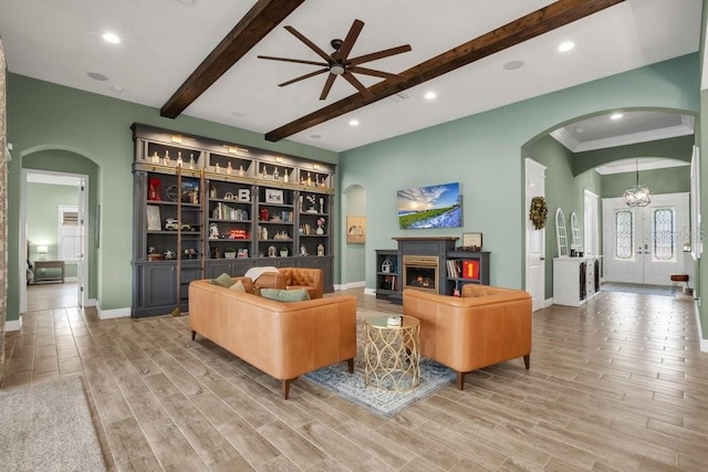 living room featuring baseboards, arched walkways, ceiling fan, beamed ceiling, and wood finished floors