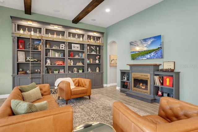 sitting room featuring a warm lit fireplace, beam ceiling, arched walkways, and wood finished floors