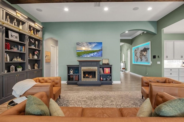 living area with baseboards, arched walkways, recessed lighting, wood finished floors, and a glass covered fireplace