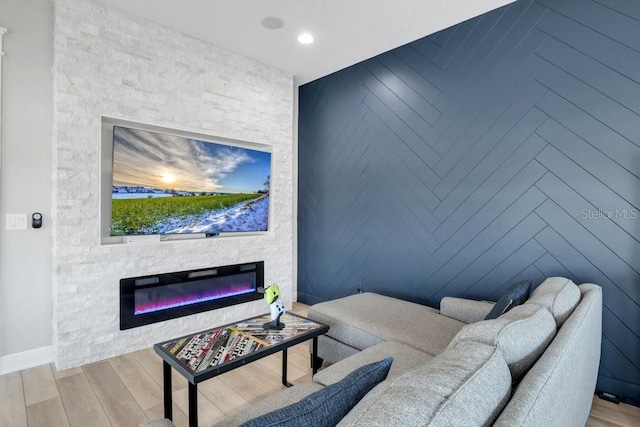 living room featuring baseboards, an accent wall, a fireplace, recessed lighting, and wood finished floors