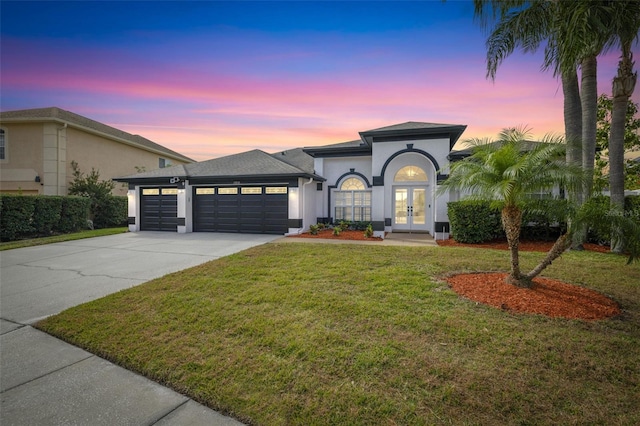 view of front facade featuring a garage, a lawn, and french doors