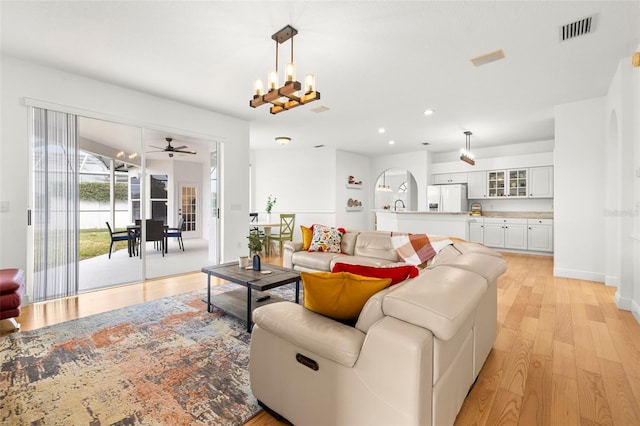 living room featuring ceiling fan with notable chandelier and light wood-type flooring