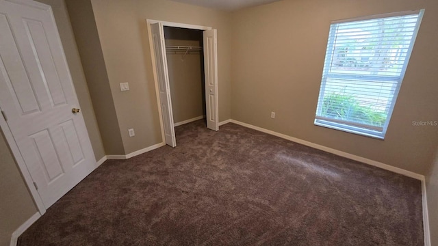 unfurnished bedroom with dark carpet and a closet