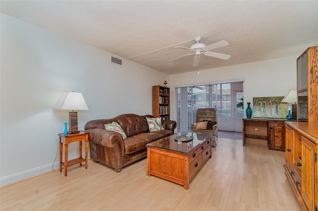 living room with a textured ceiling, ceiling fan, and light wood-type flooring