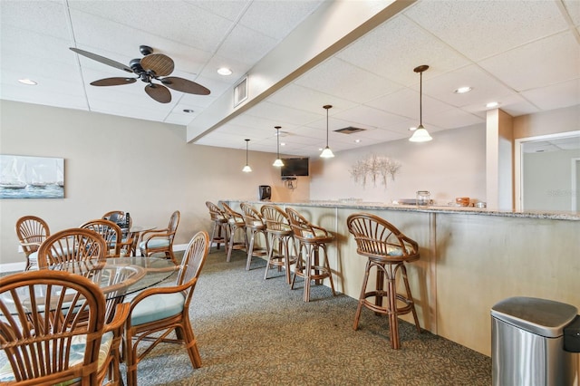 dining space featuring dark carpet, a paneled ceiling, and indoor bar