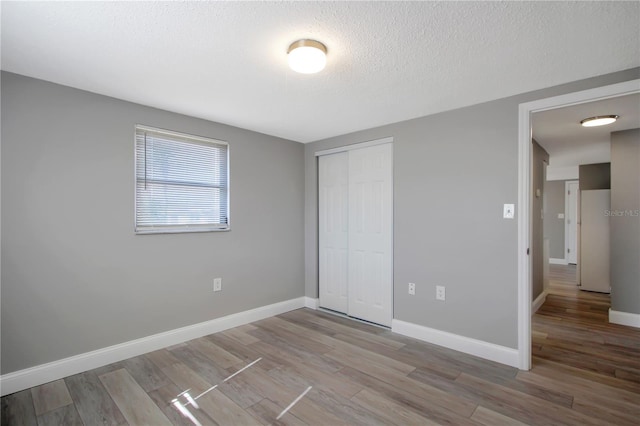 unfurnished bedroom with a textured ceiling, light wood-type flooring, and a closet