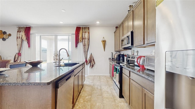 kitchen with a kitchen island with sink, sink, dark stone counters, and appliances with stainless steel finishes