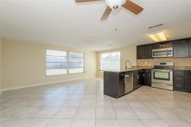 kitchen with a peninsula, a sink, appliances with stainless steel finishes, open floor plan, and backsplash