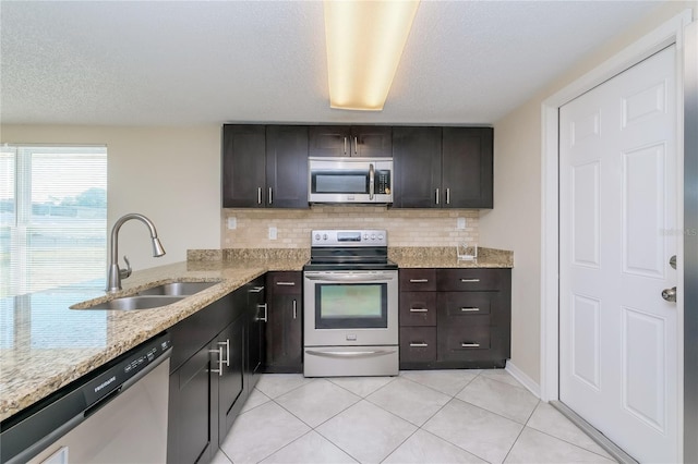 kitchen with a sink, backsplash, appliances with stainless steel finishes, and light tile patterned floors