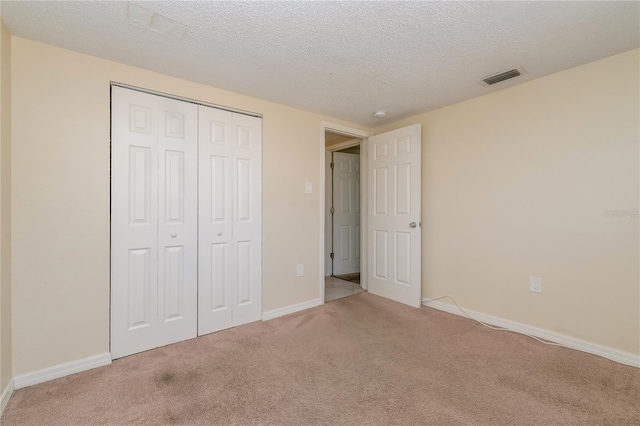 unfurnished bedroom with visible vents, a textured ceiling, a closet, carpet floors, and baseboards