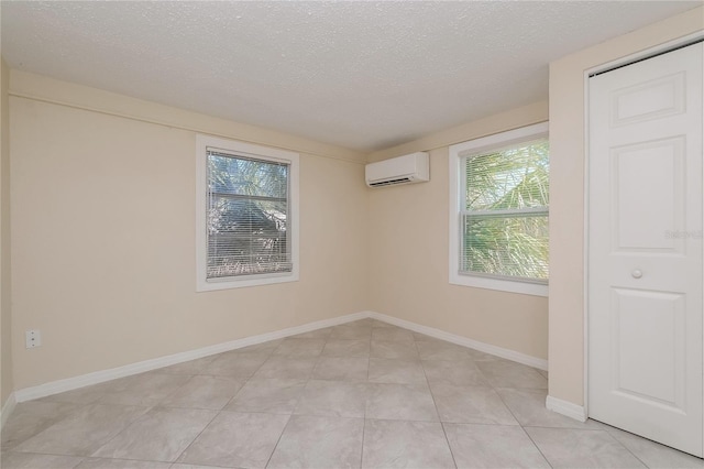 empty room featuring a wall unit AC, light tile patterned floors, baseboards, and a textured ceiling