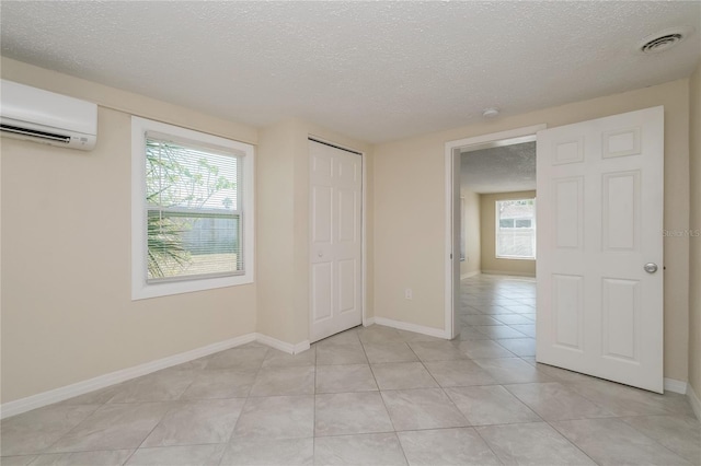 unfurnished room with a wealth of natural light, visible vents, a textured ceiling, and a wall unit AC