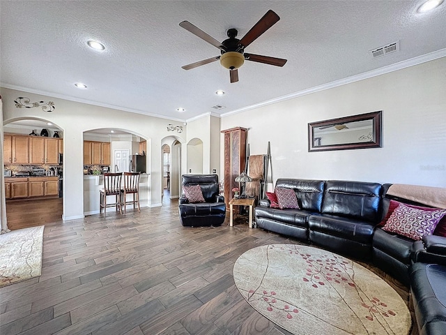 living room featuring crown molding, dark wood-type flooring, ceiling fan, and a textured ceiling