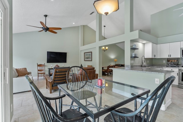 tiled dining area featuring sink, ceiling fan with notable chandelier, high vaulted ceiling, and a textured ceiling