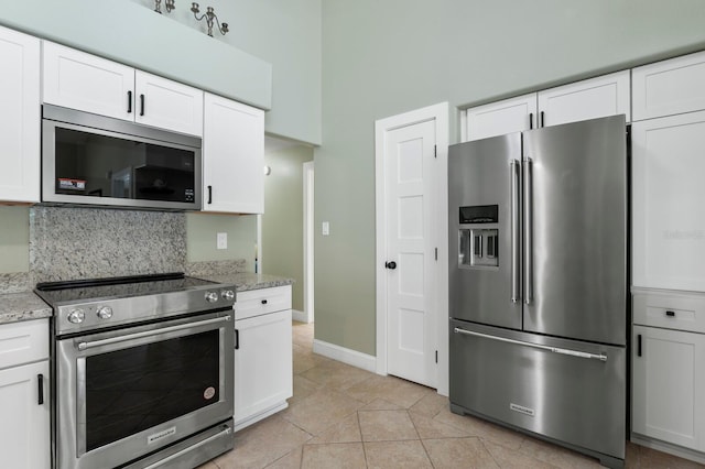 kitchen featuring light tile patterned flooring, white cabinetry, a towering ceiling, stainless steel appliances, and light stone countertops