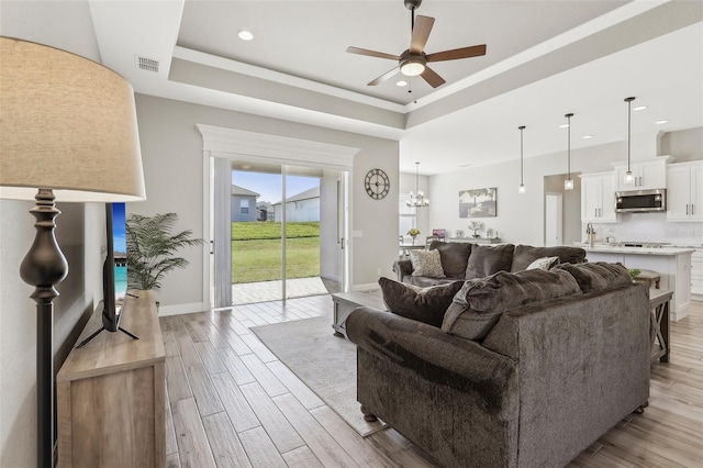 living room featuring a raised ceiling, ceiling fan with notable chandelier, and light hardwood / wood-style floors