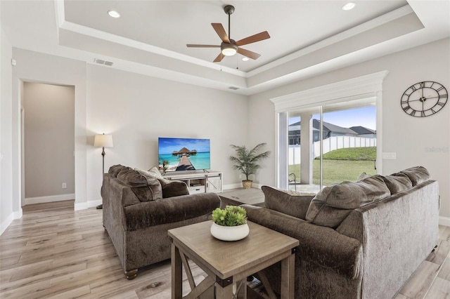 living room featuring a raised ceiling, crown molding, and light hardwood / wood-style flooring