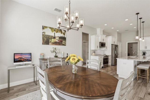 dining room featuring sink, a chandelier, and light wood-type flooring