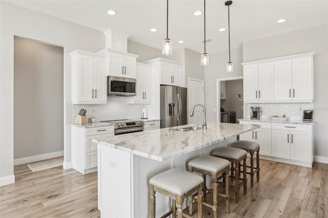 kitchen with white cabinetry, light stone counters, decorative light fixtures, appliances with stainless steel finishes, and a kitchen island with sink