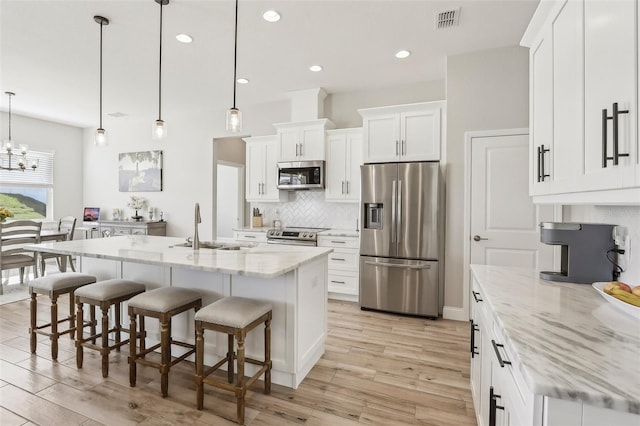 kitchen with light stone counters, white cabinetry, appliances with stainless steel finishes, and hanging light fixtures