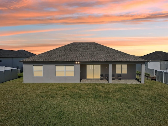 back house at dusk featuring a lawn and a patio area