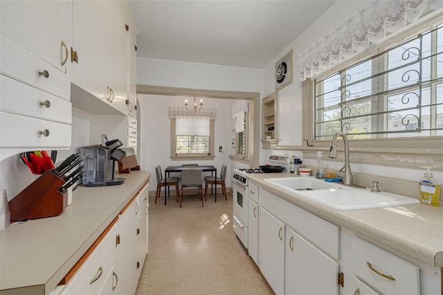 kitchen with white cabinetry, gas range oven, sink, and a notable chandelier