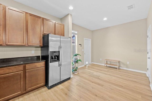 kitchen with dark stone counters, stainless steel fridge with ice dispenser, and light hardwood / wood-style flooring