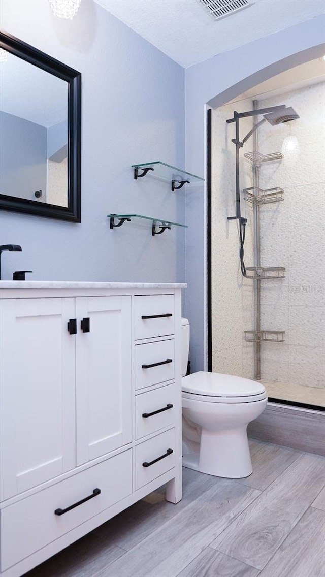 bathroom featuring vanity, wood-type flooring, a tile shower, and toilet