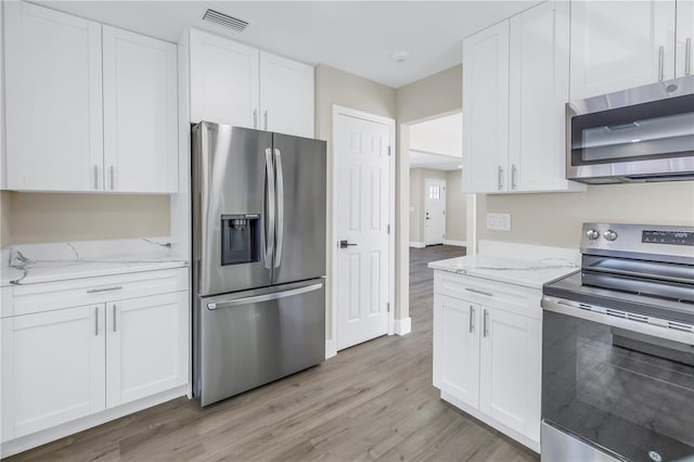 kitchen with white cabinets, light stone countertops, appliances with stainless steel finishes, and light hardwood / wood-style flooring