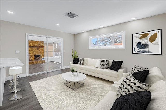 living room with a stone fireplace and dark wood-type flooring