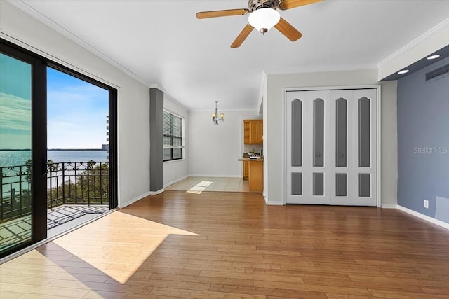 empty room featuring crown molding, hardwood / wood-style flooring, ceiling fan with notable chandelier, and a water view