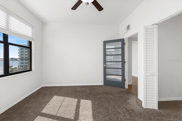 unfurnished bedroom with dark colored carpet, a water view, and ceiling fan