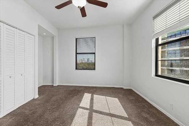 unfurnished bedroom with dark colored carpet, ceiling fan, and a closet