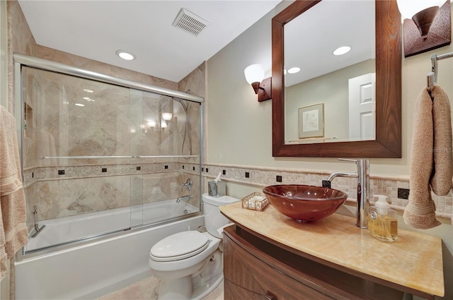 full bathroom with bath / shower combo with glass door, tile walls, vanity, and toilet