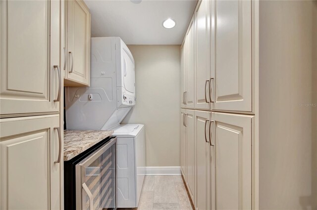 clothes washing area with beverage cooler, cabinets, and stacked washing maching and dryer