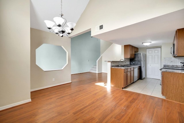 kitchen with stainless steel appliances, a sink, visible vents, backsplash, and brown cabinetry