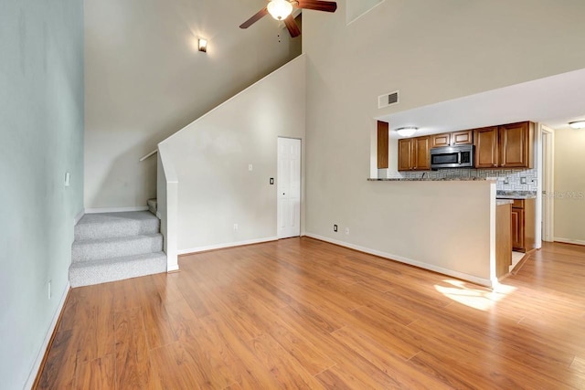 unfurnished living room featuring baseboards, visible vents, a ceiling fan, light wood-style flooring, and stairs