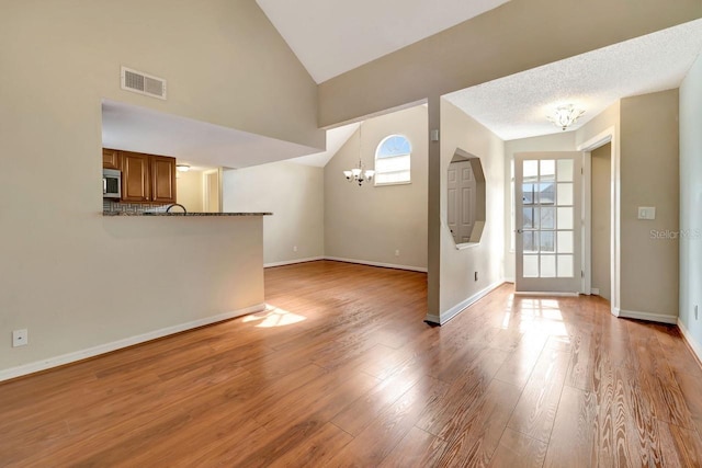 unfurnished living room featuring an inviting chandelier, vaulted ceiling, a healthy amount of sunlight, and light wood-type flooring