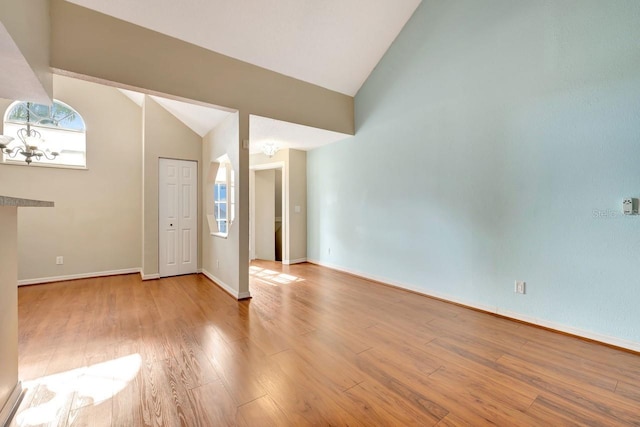 spare room with baseboards, high vaulted ceiling, wood finished floors, and an inviting chandelier