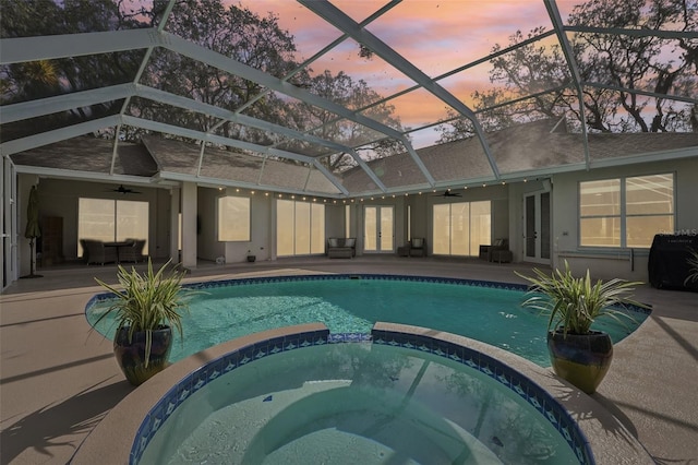 pool at dusk with ceiling fan, a patio, a lanai, and a pool with connected hot tub