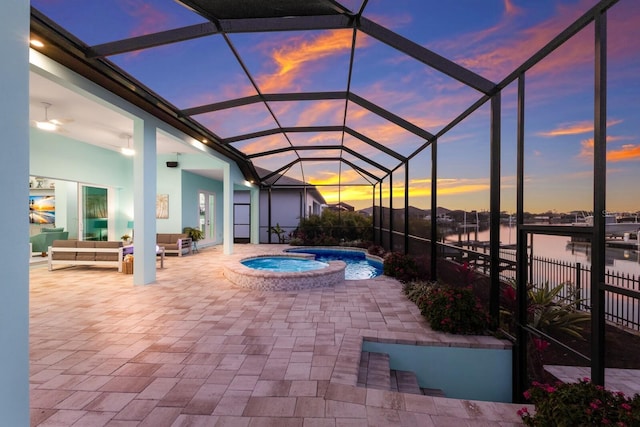 pool at dusk featuring a patio, an in ground hot tub, a lanai, an outdoor living space, and a water view