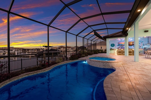 pool at dusk featuring an in ground hot tub, glass enclosure, and a patio area