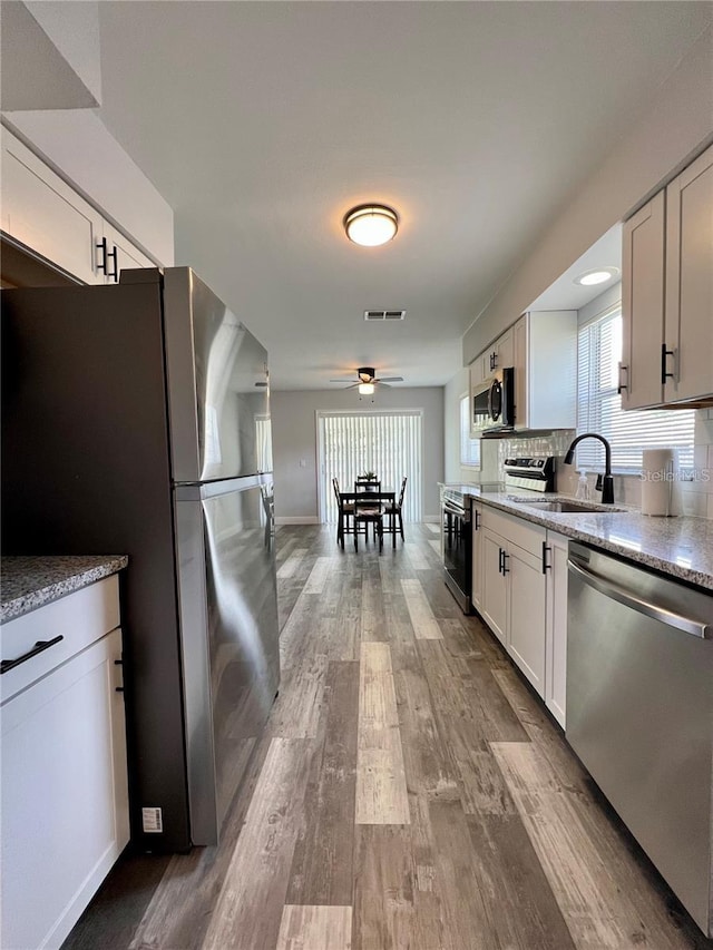 kitchen featuring sink, white cabinetry, tasteful backsplash, appliances with stainless steel finishes, and light hardwood / wood-style floors