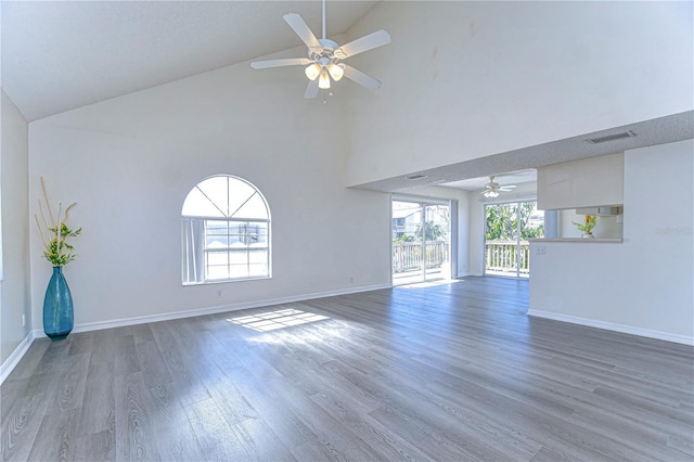 empty room with high vaulted ceiling, a healthy amount of sunlight, hardwood / wood-style floors, and ceiling fan