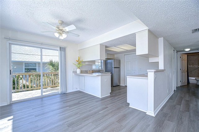 kitchen with white cabinets, dark hardwood / wood-style floors, kitchen peninsula, and stainless steel refrigerator