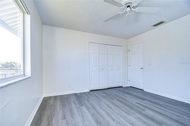 unfurnished bedroom featuring hardwood / wood-style flooring, ceiling fan, a textured ceiling, and a closet