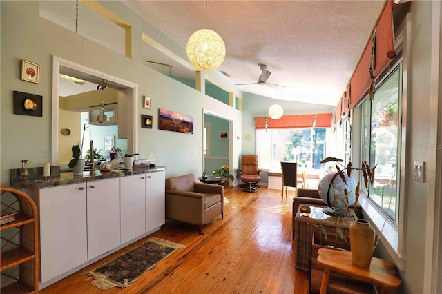 living room featuring vaulted ceiling, ceiling fan, a textured ceiling, and light hardwood / wood-style floors