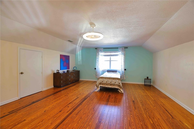 unfurnished bedroom featuring lofted ceiling, wood-type flooring, and a textured ceiling