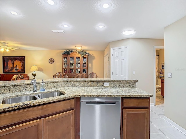 kitchen with light tile patterned flooring, stainless steel dishwasher, sink, and light stone counters