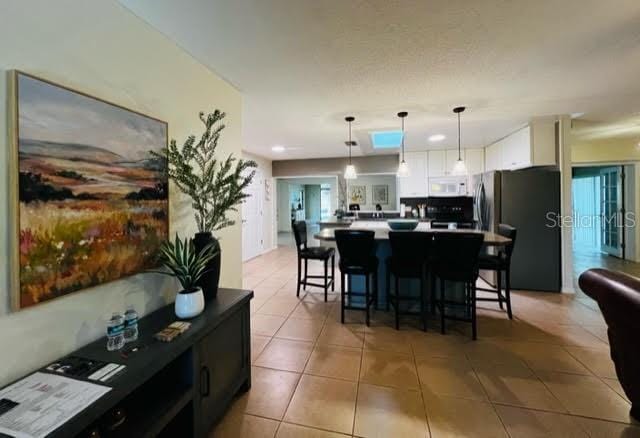 kitchen with white microwave, white cabinetry, a kitchen breakfast bar, hanging light fixtures, and freestanding refrigerator